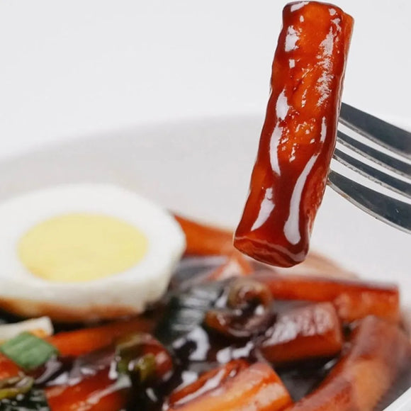 Close-up of a fork with a piece of tteokbokki on black bean sauce