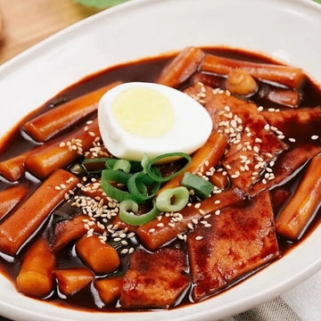 Tteokbokki on black bean sauce and a hard-boiled egg on a white plate.