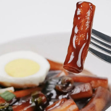Close-up of a fork with a piece of Tteaokbokki in black bean sauce with an egg and vegetables.