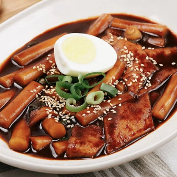 Tteaokbokki in black bean sauce with a hard-boiled egg on a white plate