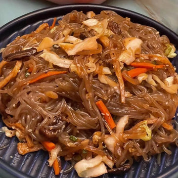 A plate of Japchae, which consists of sweet potato noodles stir-fried with vegetables and ground pork, commonly served in Korea.