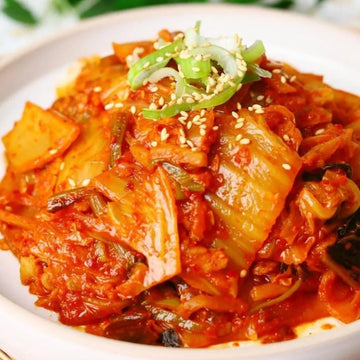 Kimchi dish with red sauce, green onions, and sesame seeds on a white plate.