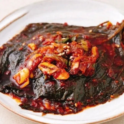 A plate of Korean perilla side dish (kkaenip-muchim) with visible chili flakes, seeds, and a mix of ingredients.