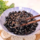 Bowl of black beans with a pair of chopsticks holding a bean.