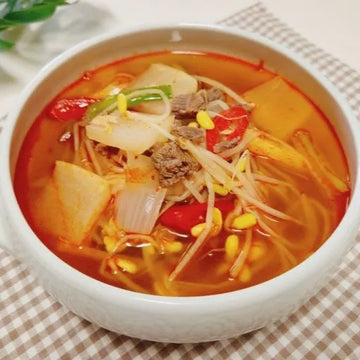 Bowl of Korean soup with tofu, vegetables, and meat on a checkered tablecloth
