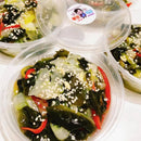 Container of seaweed salad with sesame seeds on a white surface