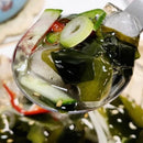 Spoonful of sweet and sour seaweed salad, pickled vegetables including cucumbers and radishes with a clear liquid.
