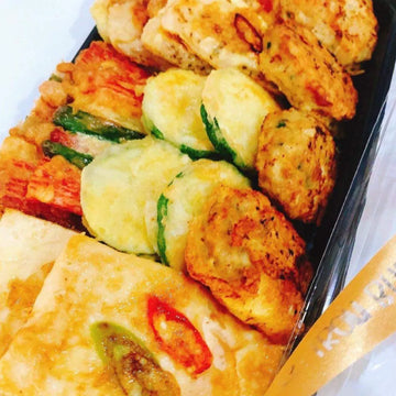 Assorted Korean Pancake snacks including breaded items and vegetables on a black tray.