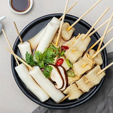 Mul-tteok, skewered vegetables in a black bowl on a light background