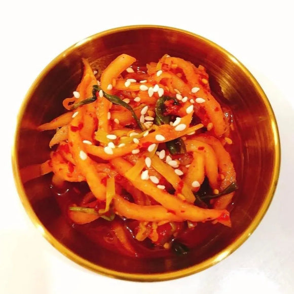 Spicy fermited radish with sesame seeds in a metallic bowl on a white background