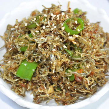 A plate of Myeolchi Bokkeum, which is stir-fried dried anchovies with green peppers and sesame seeds on top.