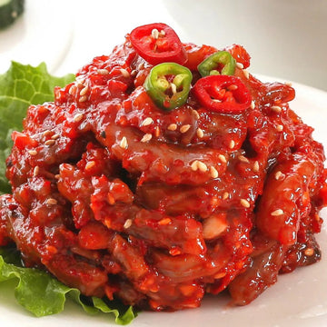 A plate of Korean fermented octopus dish, nakjijeot, garnished with sesame seeds and sliced chili peppers.