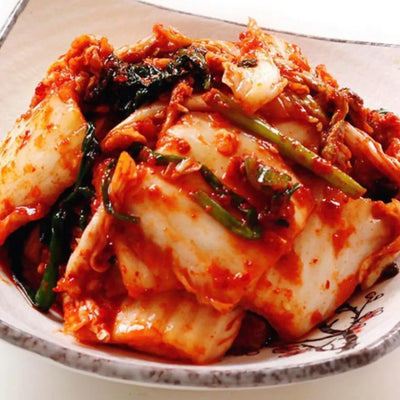 A plate of napa kimchi featuring crisp cabbage leaves in a bright red spicy sauce, garnished with scallions.