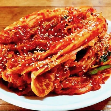 Kimchi on a white plate with sesame seeds on a wooden surface