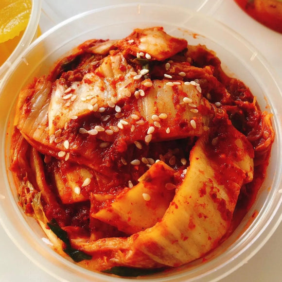 A plate of napa kimchi with a red and spicy looking sauce, garnished with green scallions.