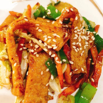 Korean stir-fried fish cakes with sliced vegetables, garnished with sesame seeds, on a plate.