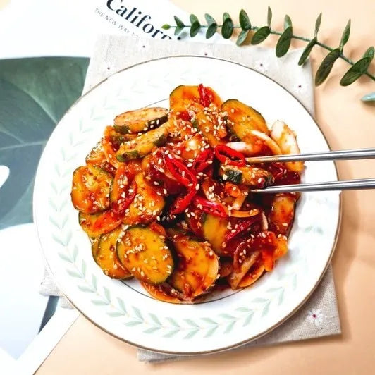 Bowl of spicy vegetable dish with chopsticks on a magazine with green leaves.