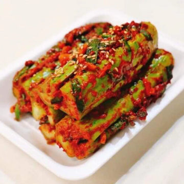 A plate of stuffed cucumber kimchi with visible spicy seasoning and herbs.