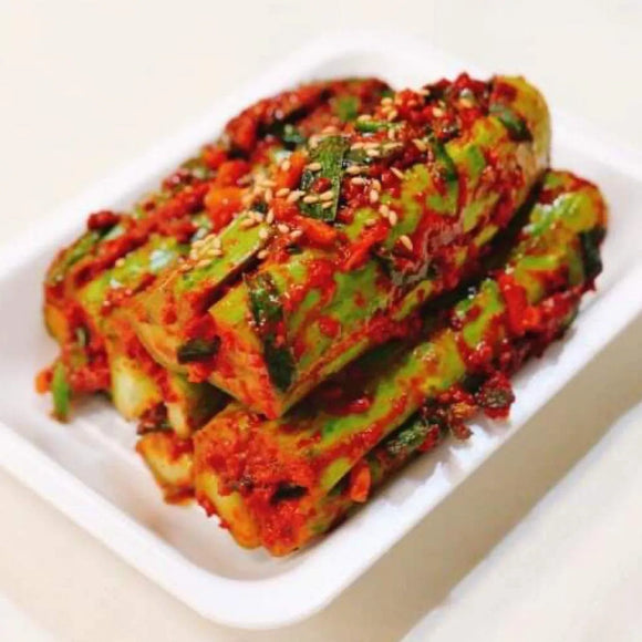 A plate of stuffed cucumber kimchi with visible spicy seasoning and herbs.