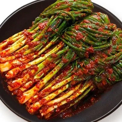 A plate of Pa-kimchi, which consists of green onions/scallions in a spicy red sauce.