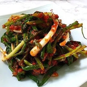 Spicy vegetable dish with green leaves and red peppers on a white plate