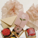 Decorative boxes with edible pressed flowers, a pink card with a white flower, and a gold envelope on a white background.