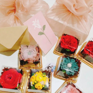 A set of variously designed edible gift items, each with a floral decoration on top, presented in a box with a greeting card.