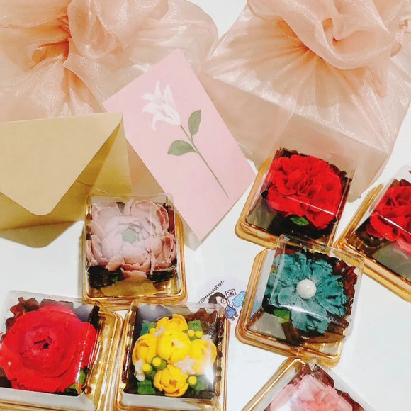 A set of variously designed edible gift items, each with a floral decoration on top, presented in a box with a greeting card.