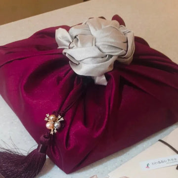 Purple fabric pouch with decorative flower and tassel on a light surface