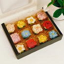 Box of colorful flower-shaped rice cakes on a white surface with a plant in the background