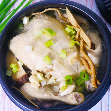 A bowl of Samgyetang, which is a whole chicken cooked with ginseng, garlic, jujube, and other herbs, garnished with green onions.