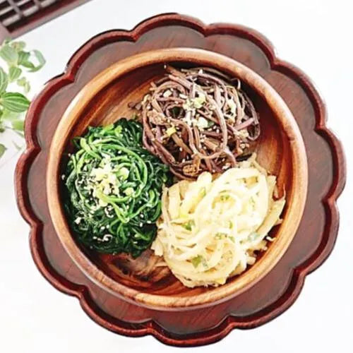 A wooden bowl containing three different side dishes consisting of white, black/brown, and green colors, representing a traditional Korean meal setup.