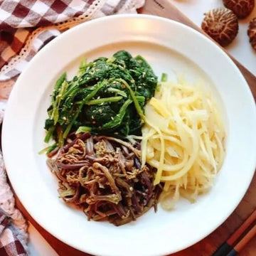 Plate of food with greens, noodles, and meat on a checkered tablecloth.