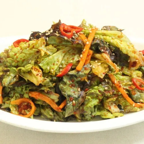 Korean lettuce salad with greens, carrots, and red peppers on a white plate.
