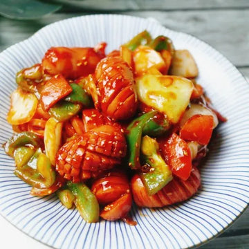 A plate of Korean banchan, featuring stir-fried Vienna sausages with colorful bell peppers, scallions, and carrots, coated in a sauce.