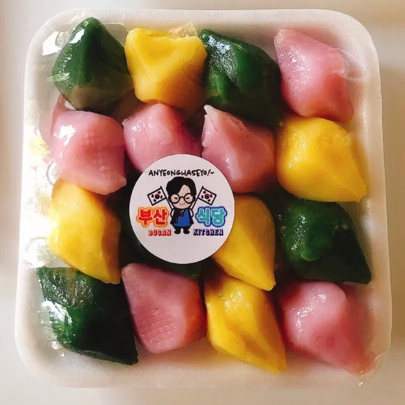 Halfmoon colorful rice cakes filled with ground sessame in a container with a brand label on a white background