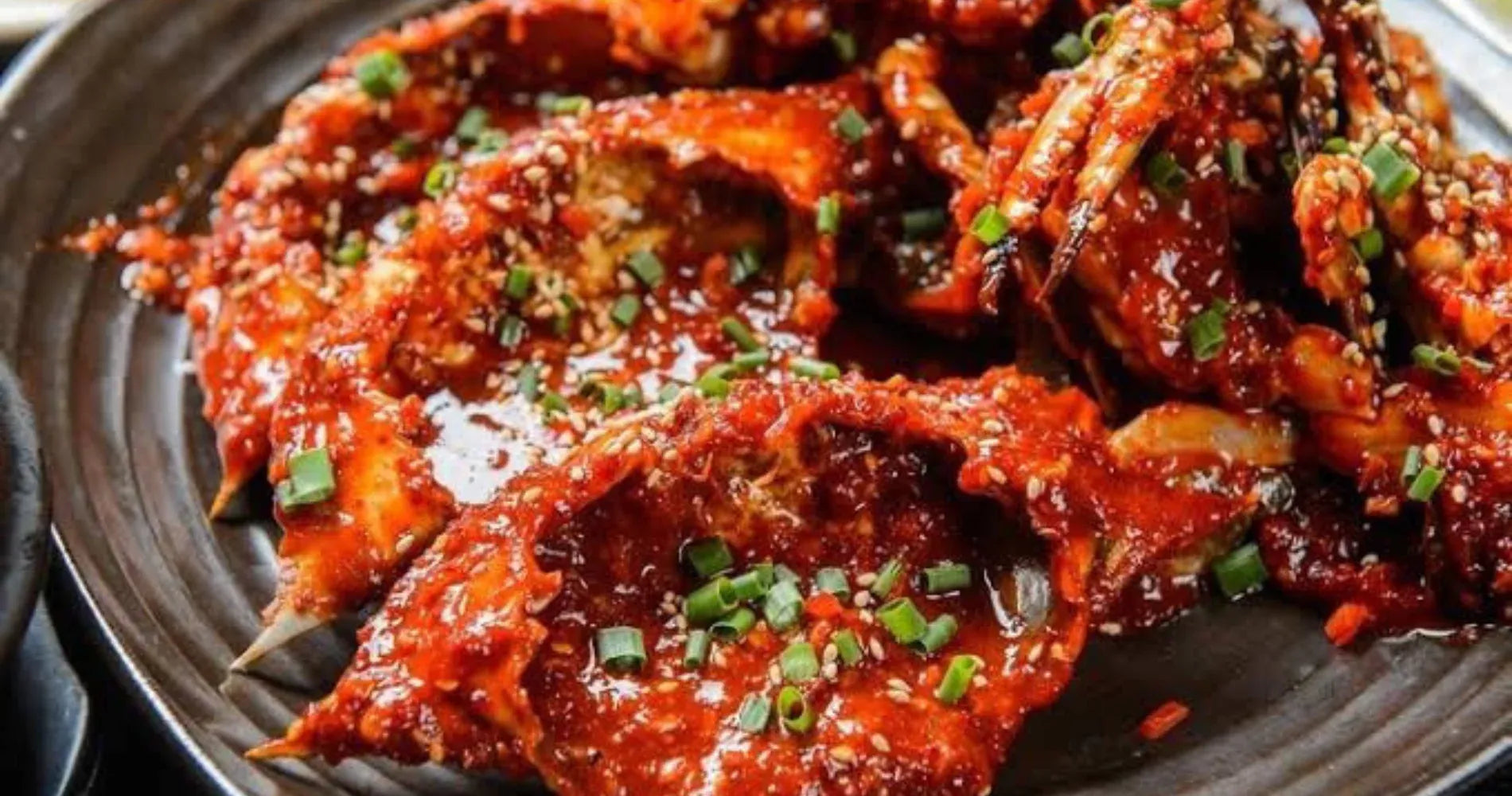 Spicy crab dish with red sauce and green onions on a dark plate