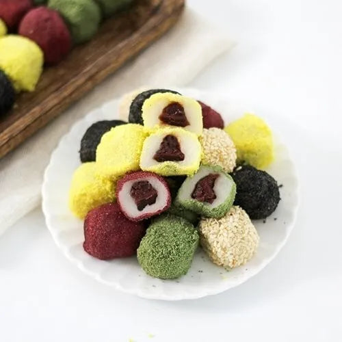 Gyeongdan. Assorted colorful rice balls on a white plate with a wooden tray in the background.