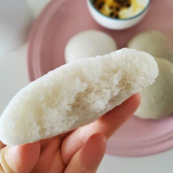 Close-up of a hand holding a piece of alcohol rice cake with a pink plate and more rice cakes in the background.