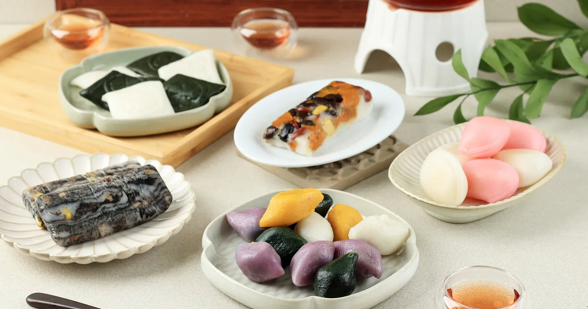 Assorted colorful rice cakes on a table with tea cups and a teapot.