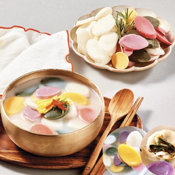 A prepared Tteok Mandu-gguk (soup kit) served in a bowl with colorful rice cakes and garnishes on the side.