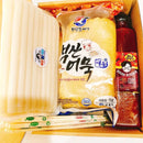 Packaged tteokbokki including rice noodles, a bottle of sauce, and sticks in a box.