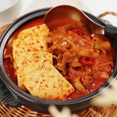 Kimchi stew with tofu and meat in a black bowl on a woven mat