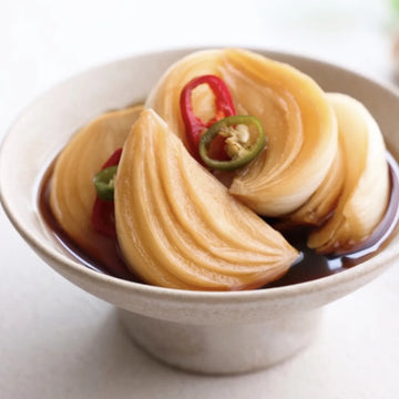 Bowl of pickled onion with red and green chili slices on a white background