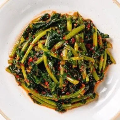 A plate of Yeulmu Kimchi, a Korean side dish made from young radish greens with a garnish of red chili flakes.