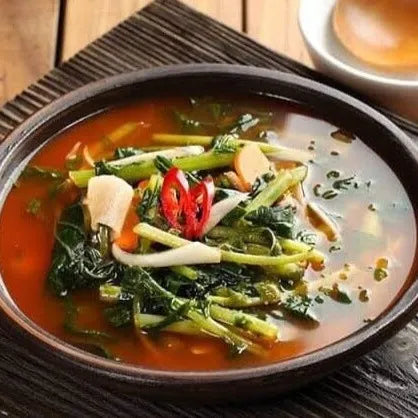 A bowl of Yeulmu Mulkimchi, which consists of young radish leaves in a soupy broth, garnished with sliced radish and chili peppers.