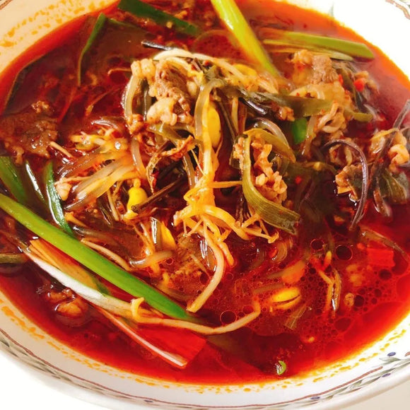 A bowl of Yukgaejang soup, featuring sliced beef, glass noodles, and various vegetables served in a spicy red broth.